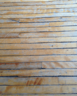 A close-up photo of an old, weathered oak floor with peeling and worn finish, and visible signs of age. The wood is crooked, sloped, and faded, adding to the rustic charm of the image.